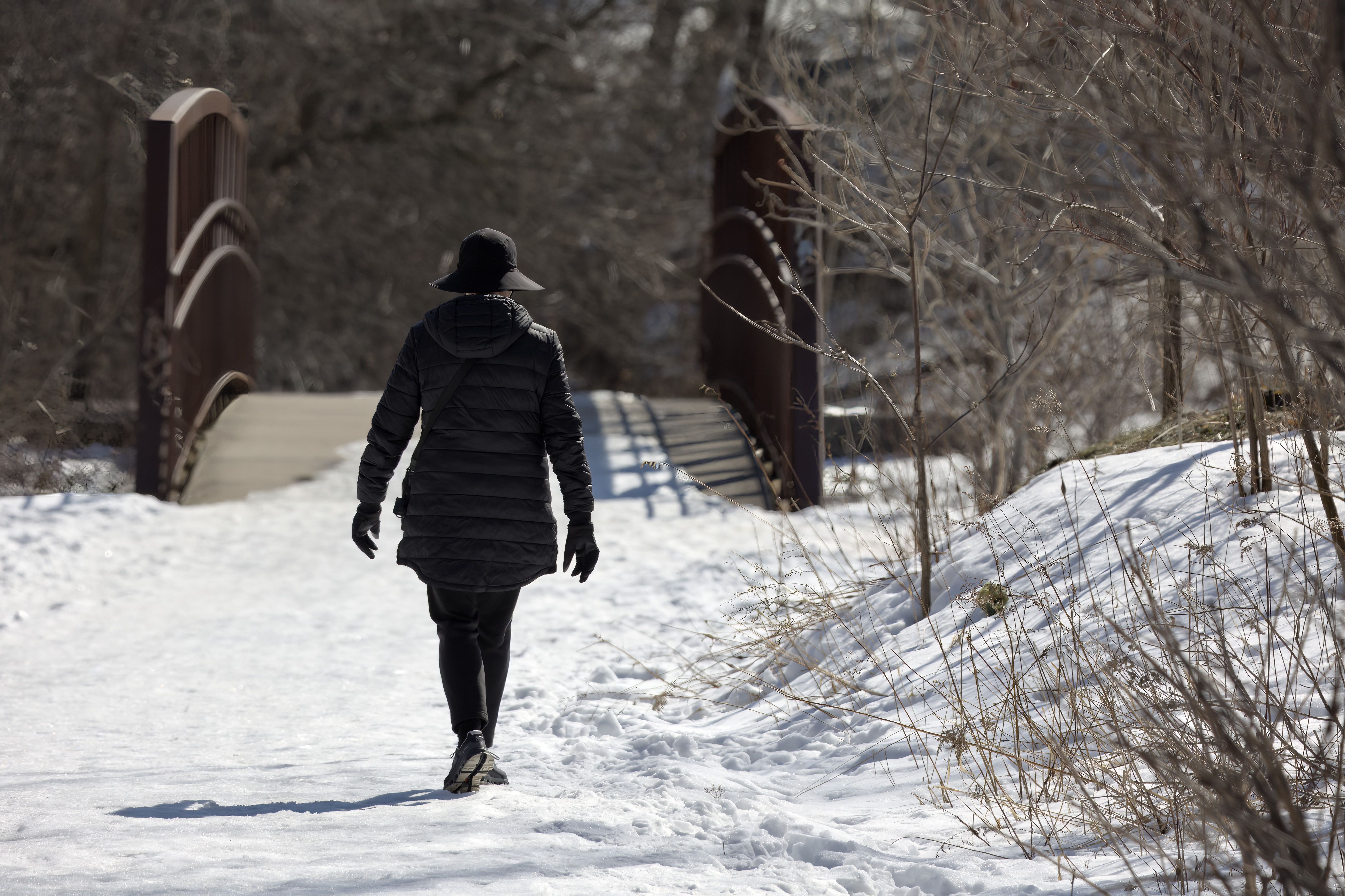 A woman walks on a snowy path over a bridge in a winter park in Toronto, Canada.