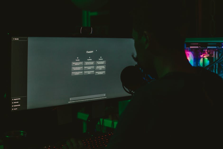 A man using a computer with a large screen in a dark room, focused on technology.
