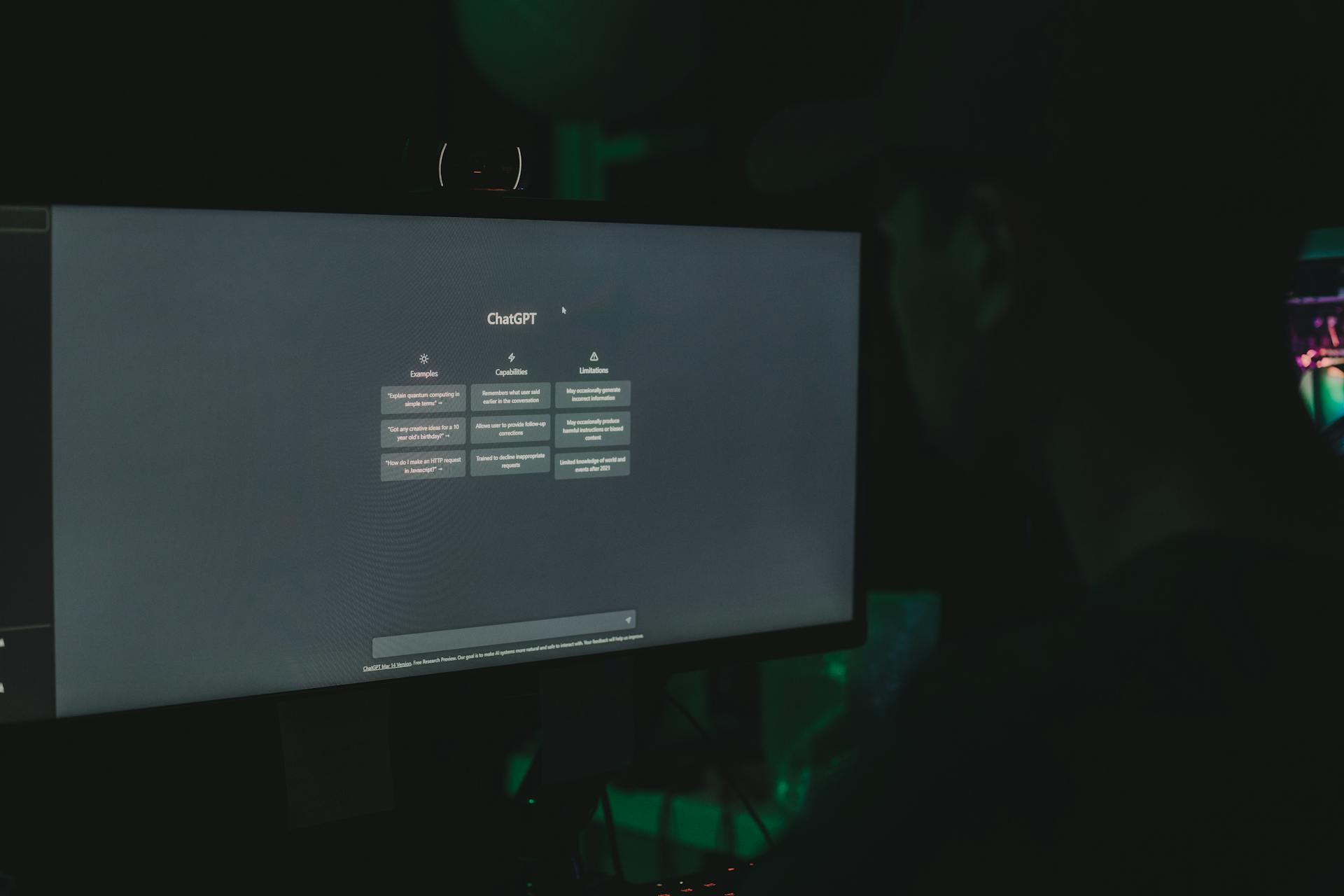 A person interacting with ChatGPT interface on a computer screen in a dimly lit room.