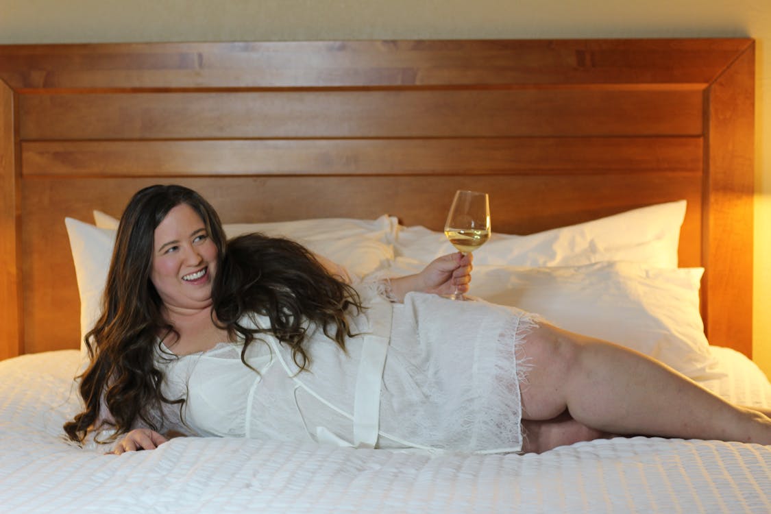 Woman Lying in Bed and Holding a Glass of White Wine 