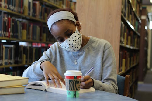 Woman in Mask Writing in Book