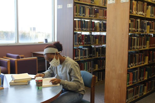 Woman in Mask Sitting in Library