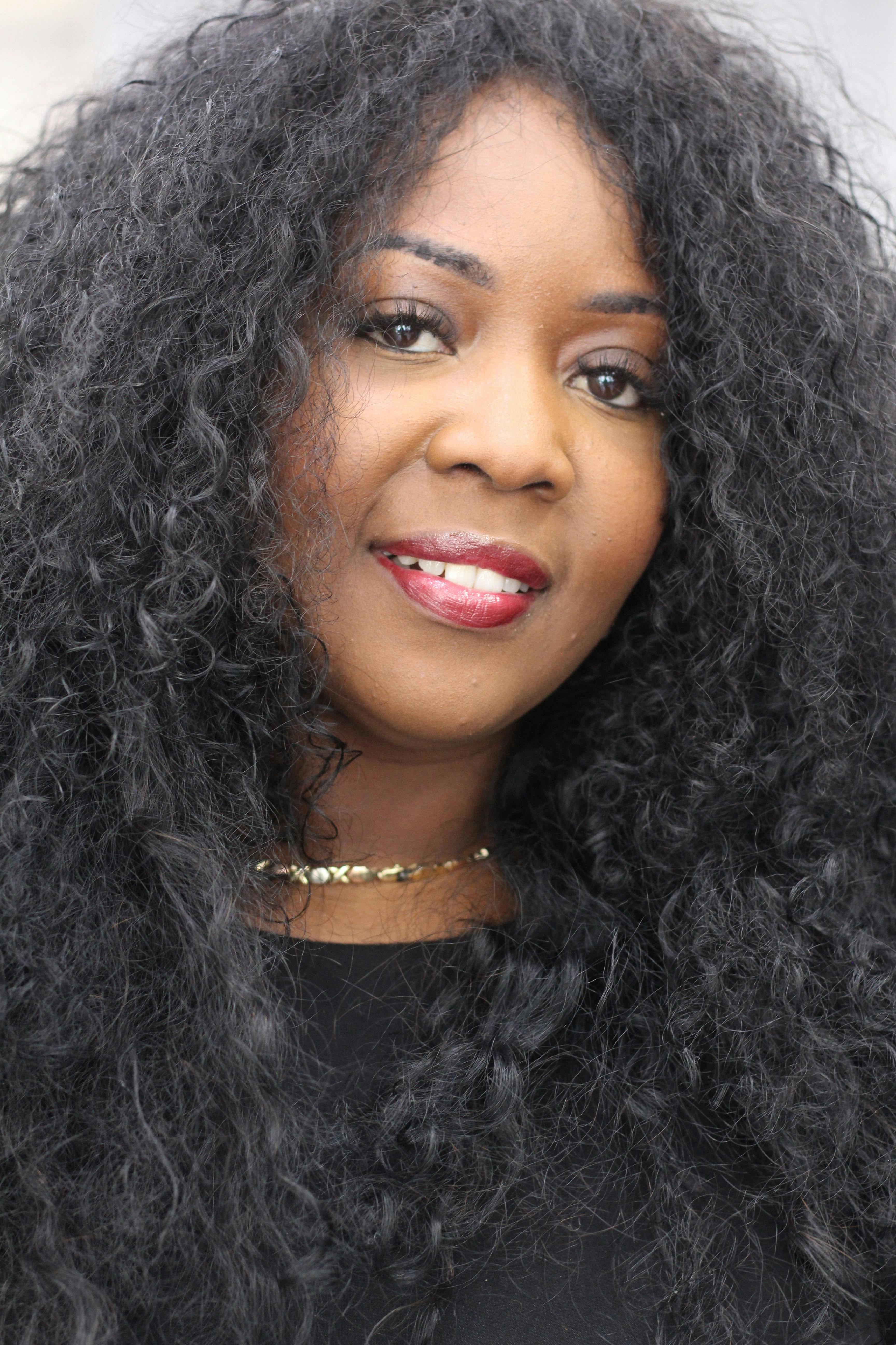 Close-up portrait of a confident woman with long curly black hair and red lipstick.