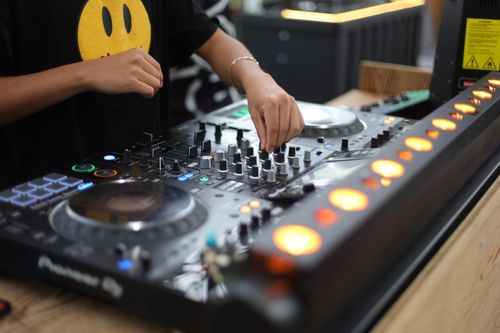 Free DJ adjusting controls on a sound mixer with vibrant lights, creating an engaging music experience. Stock Photo