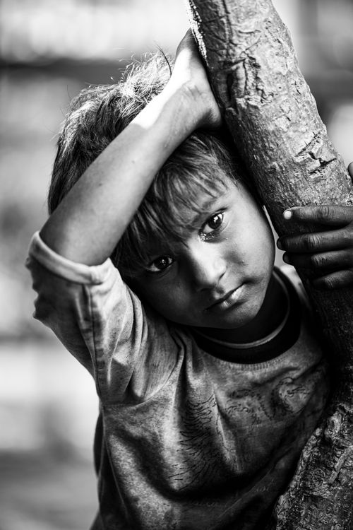 Free Black and white portrait of a South Asian boy leaning on a tree, capturing childhood innocence. Stock Photo