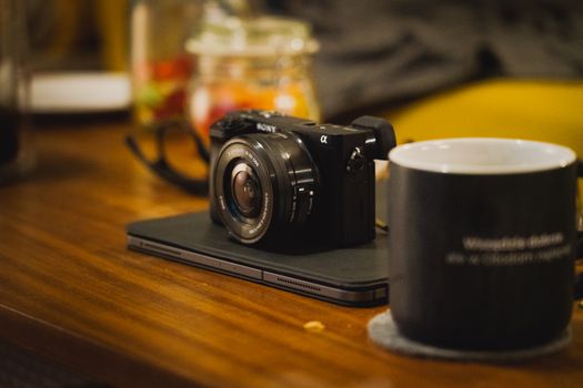 Close-up of a mirrorless camera and coffee cup on a wooden desk indoors.