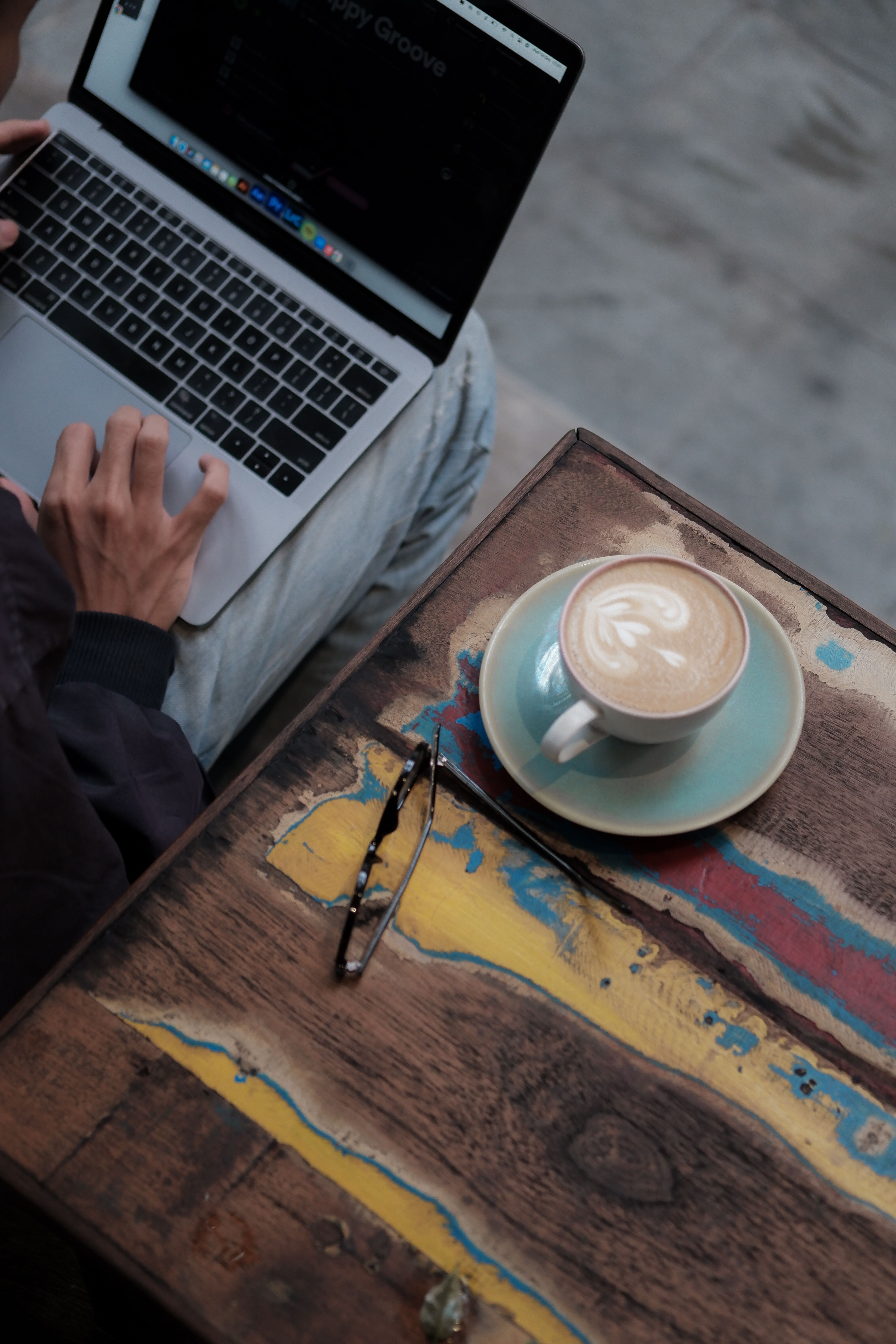 High-angle view of a person working remotely on a laptop with a cup of coffee on a vibrant-colored table.