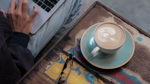 High-angle view of a person working remotely on a laptop with a cup of coffee on a vibrant-colored table.