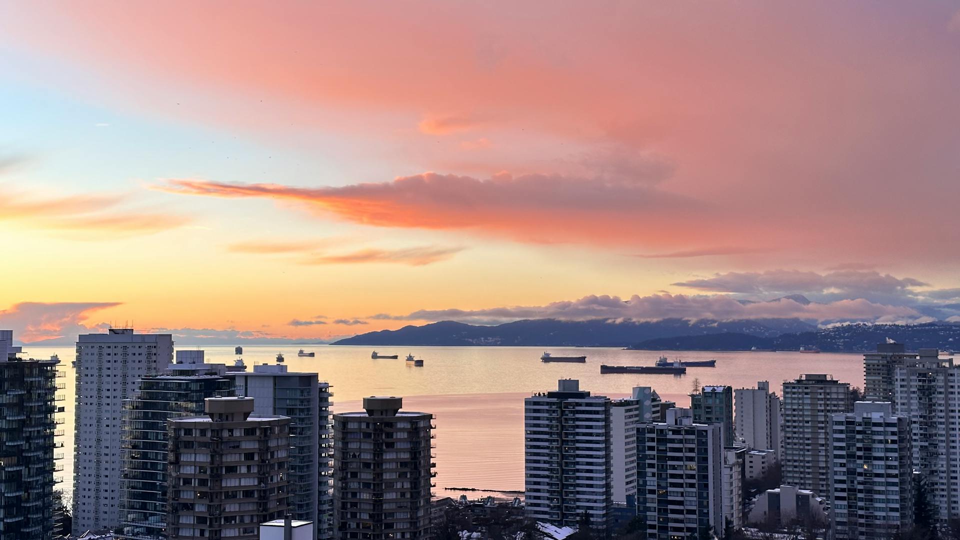 Aerial view of Vancouver skyline with ships in harbor during a vibrant sunset.