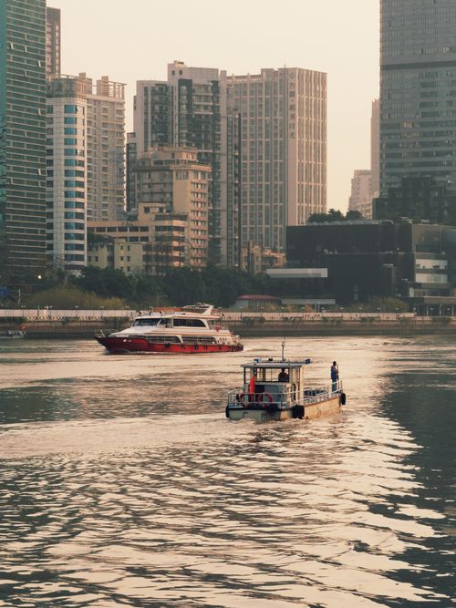 Free View of a bustling city skyline with boats navigating a river at sunset. Stock Photo
