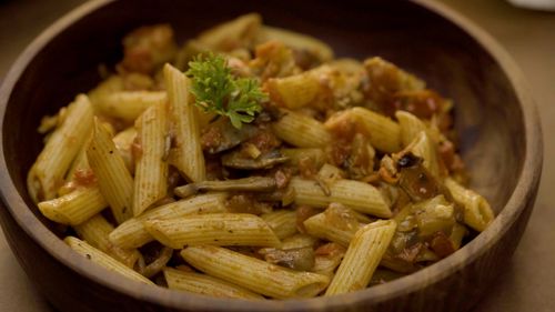 Free Close-up of flavorful penne pasta with mushrooms, tomatoes, and herbs served in a wooden bowl. Stock Photo
