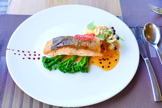 Gourmet salmon dish elegantly presented with greens, mushrooms, and sauce.
