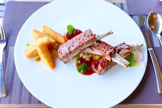 Delicious barbecued pork ribs with potato wedges on a white plate.
