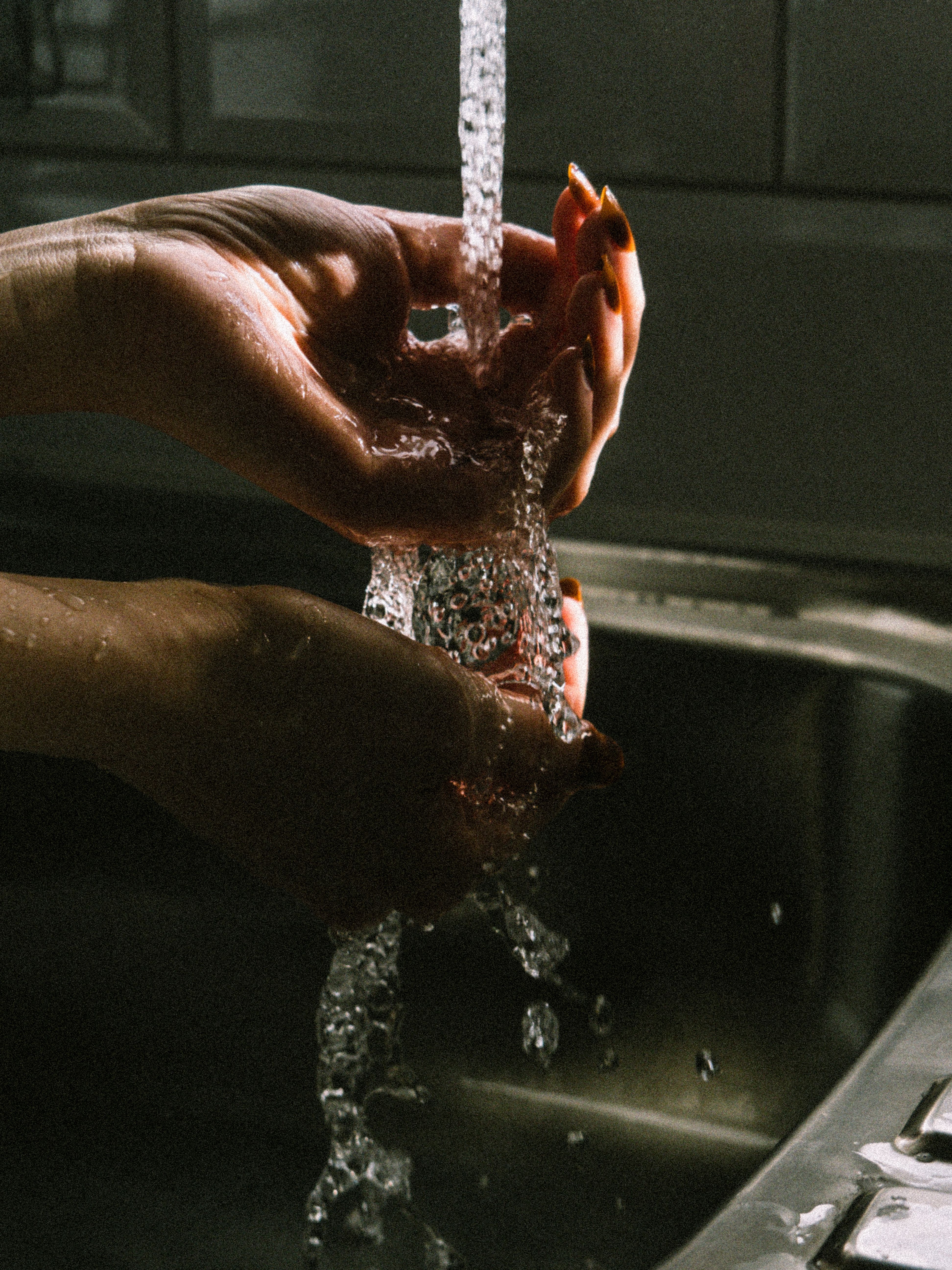 Detailed view of hands washing under a stream of water in a sink, highlighting hygiene practice.