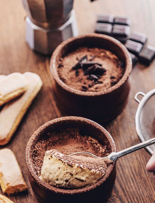 Free High-angle view of rich chocolate mousse in ceramic bowls, garnished with cocoa, on a wooden table with ladyfingers. Stock Photo