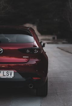 Stylish red Mazda hatchback captured from behind on a quiet road.