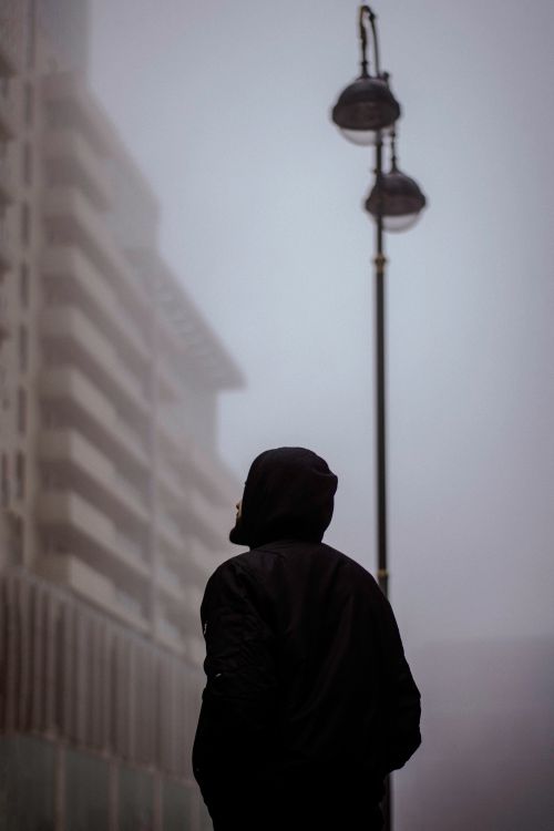 Free A person in a black hooded sweatshirt gazes at a street lamp enveloped in fog in Baku, Azerbaijan. Stock Photo