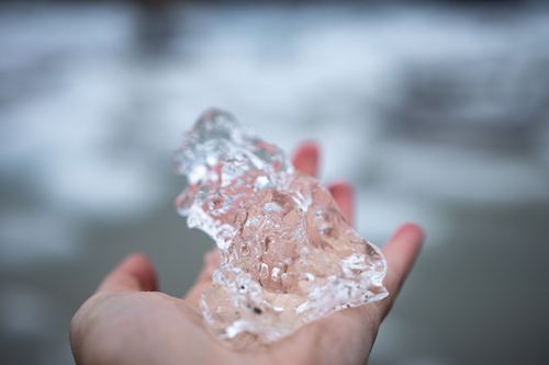 Free Close-up of a hand holding a piece of clear ice against a blurred natural backdrop. Stock Photo