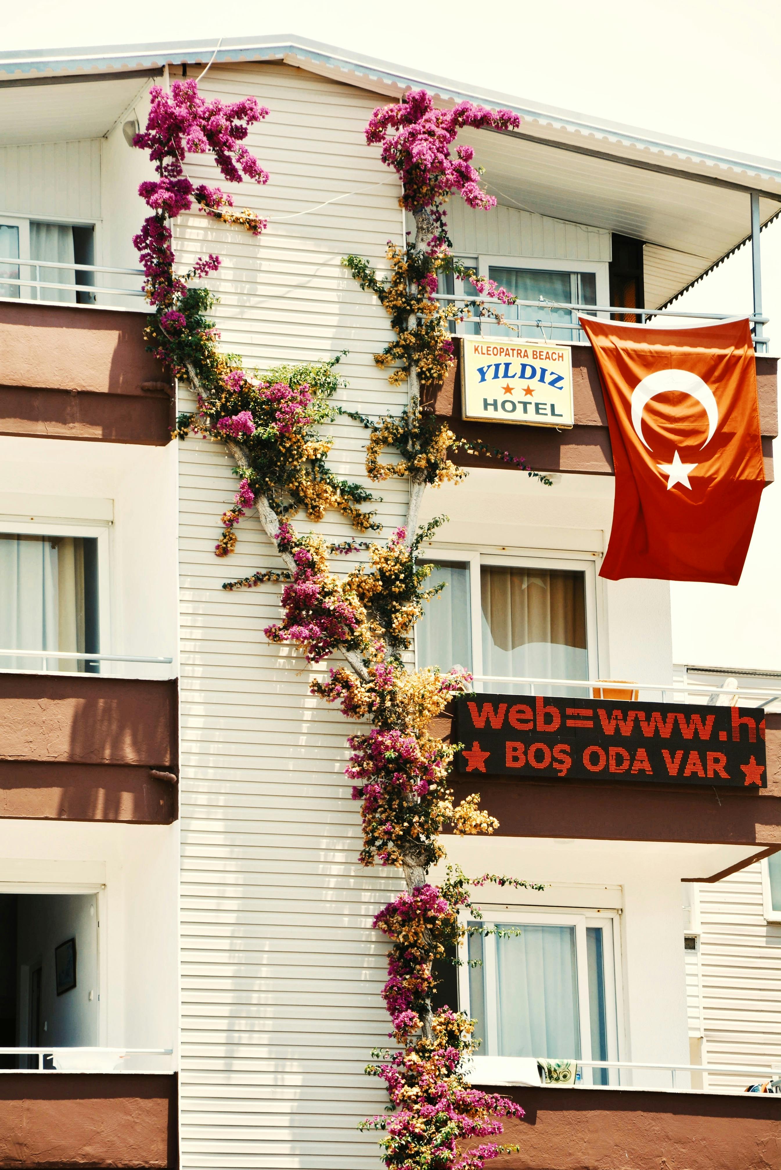 Charming hotel facade in Türkiye featuring balconies, plants, and a national flag.
