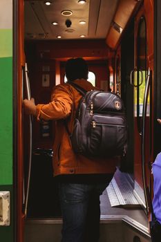 A man with a backpack boards a vehicle, captured from behind in an interior setting.