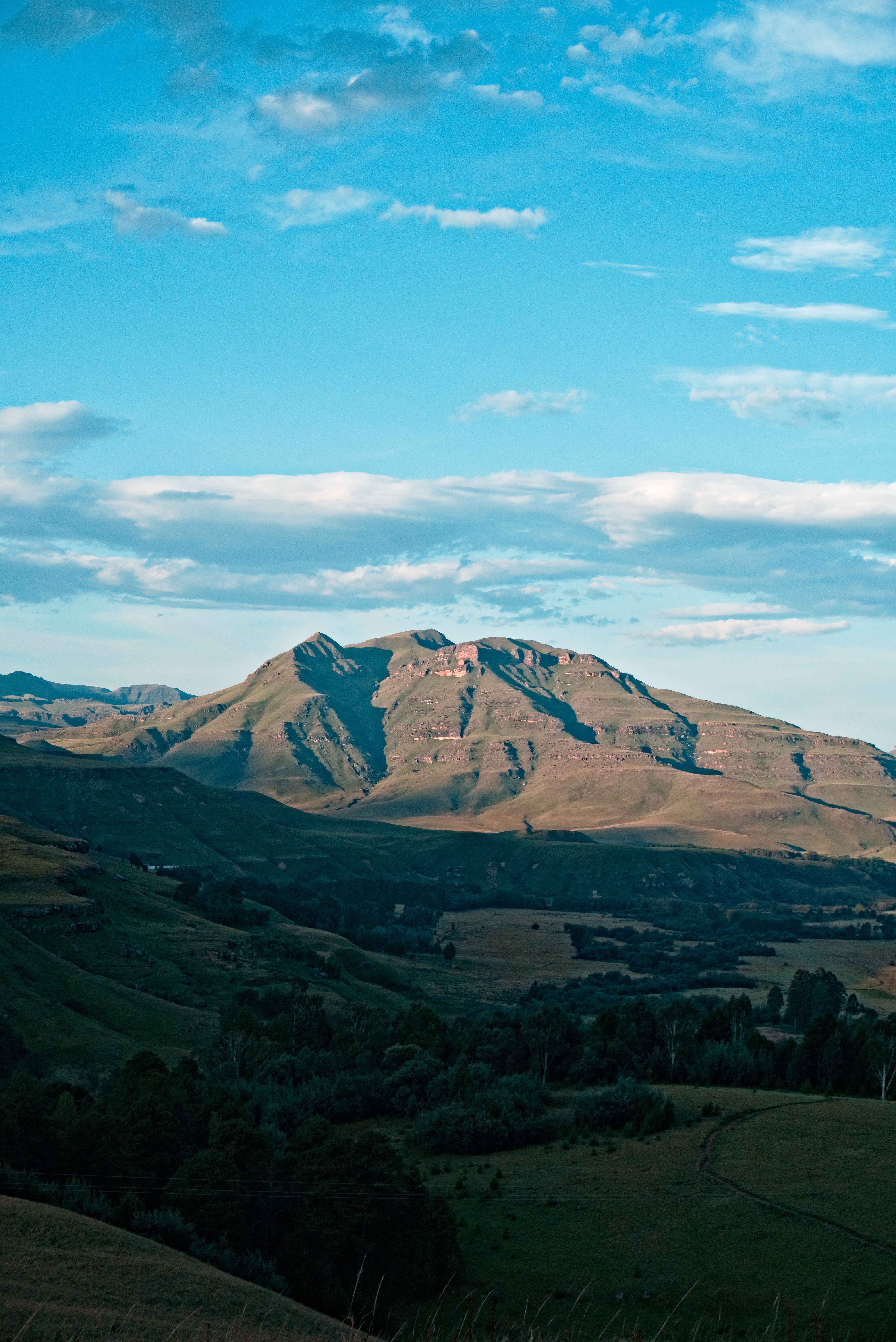 Breathtaking view of a mountain range under a clear blue sky with soft clouds and a lush green valley.