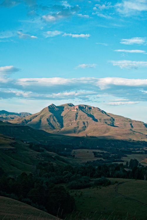 Free Breathtaking view of a mountain range under a clear blue sky with soft clouds and a lush green valley. Stock Photo