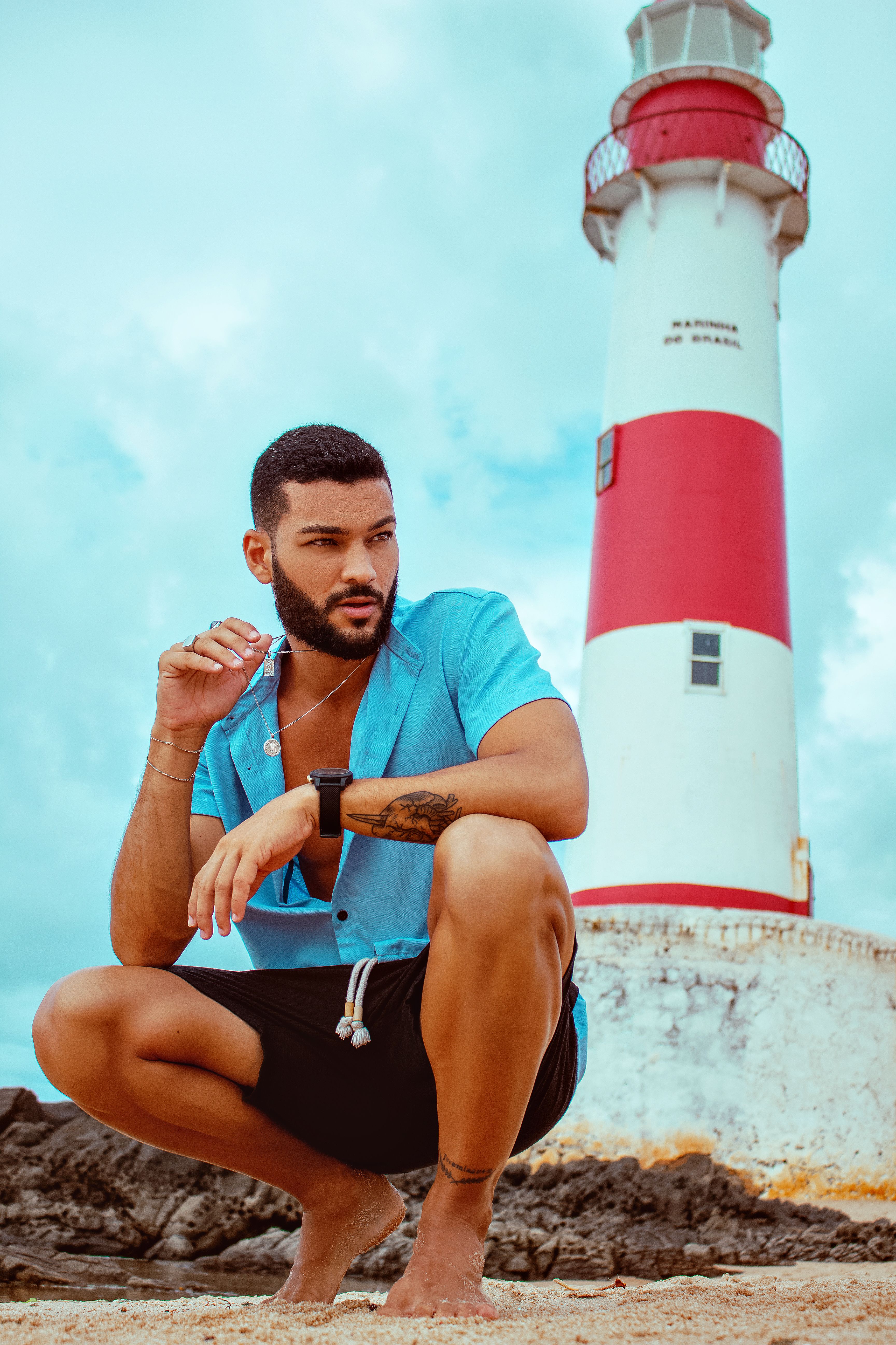 Man in blue shirt crouching by a lighthouse in Salvador, Brazil.