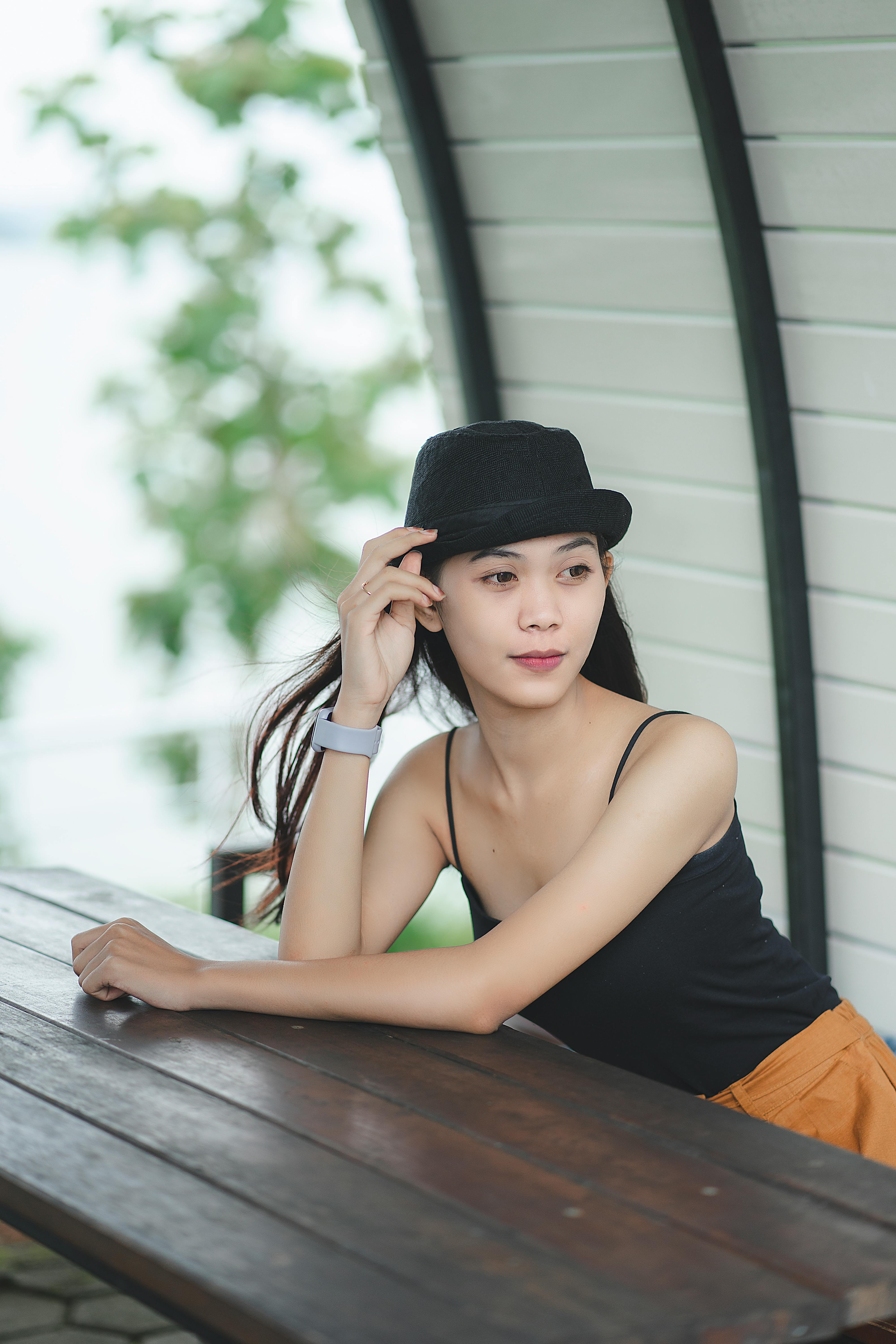 Elegant Asian woman in hat sitting outdoors on a bench in Bandung, Indonesia.