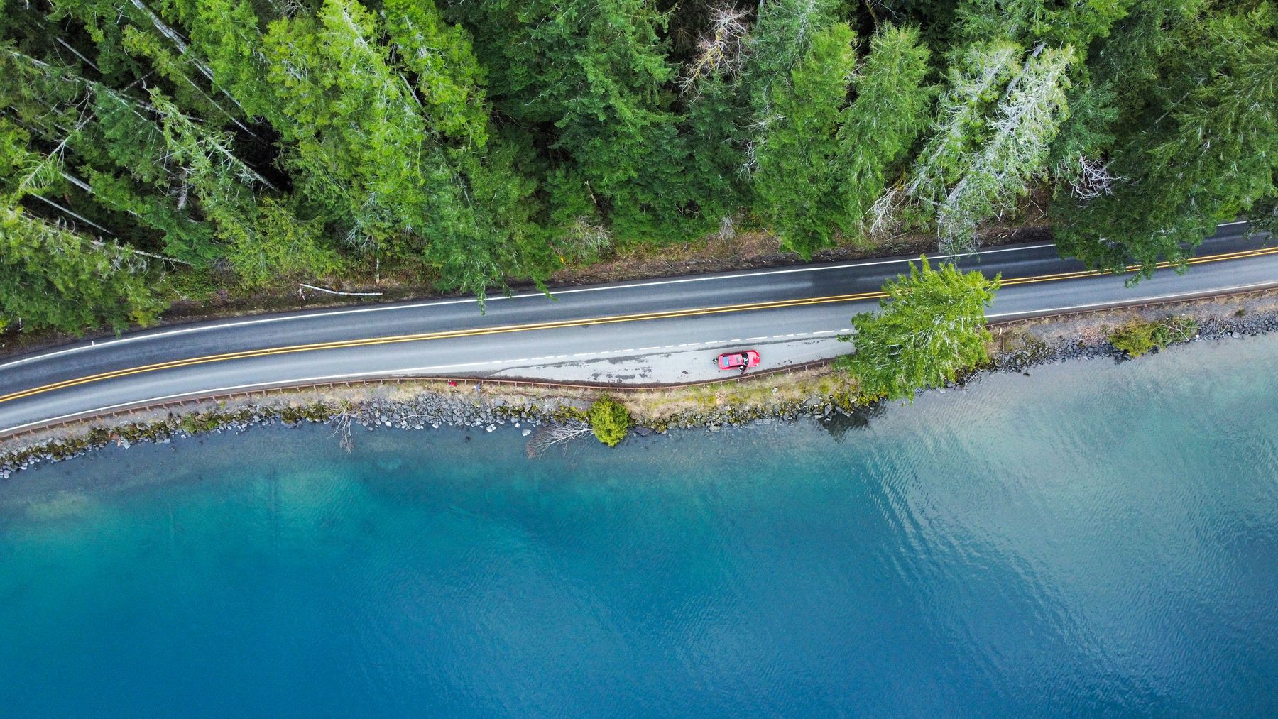 Aerial view of a car parked beside a lakeside forest road — photo by jayjay13 on Pexels