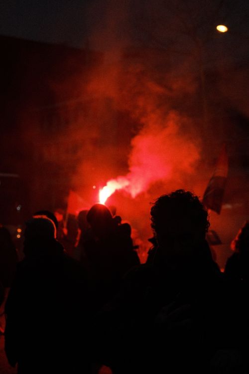 Free Silhouetted protest crowd with a red flare creating smoke at night, evoking strong emotions. Stock Photo