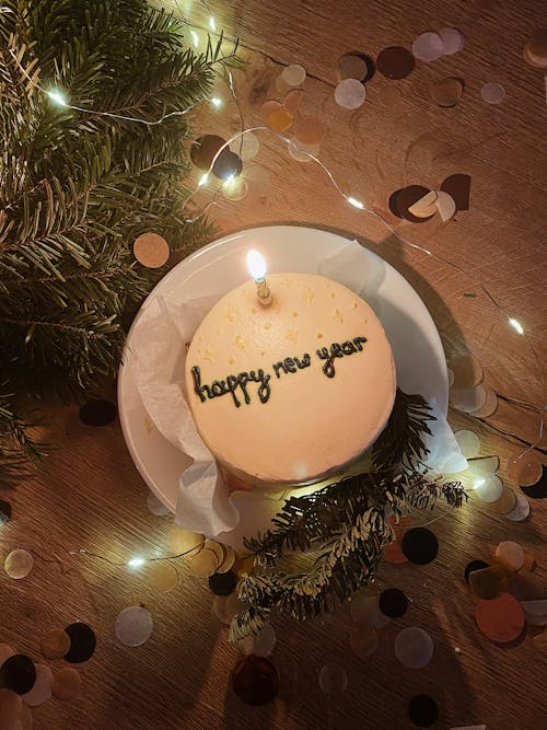 Cake with the inscription Happy New Year with a burning candle on the background of lights and confetti