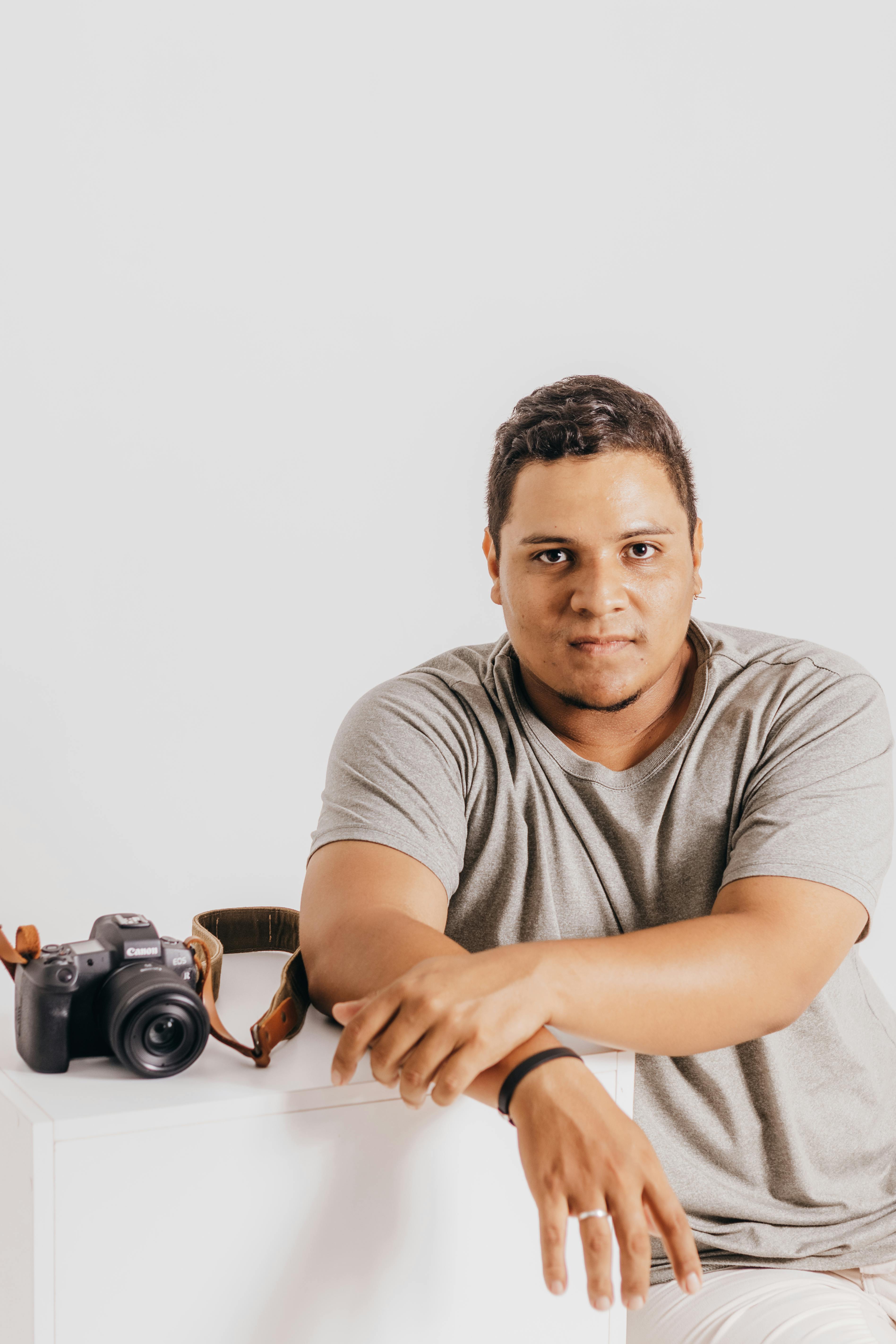 Portrait of a young man with a DSLR camera on a white background.
