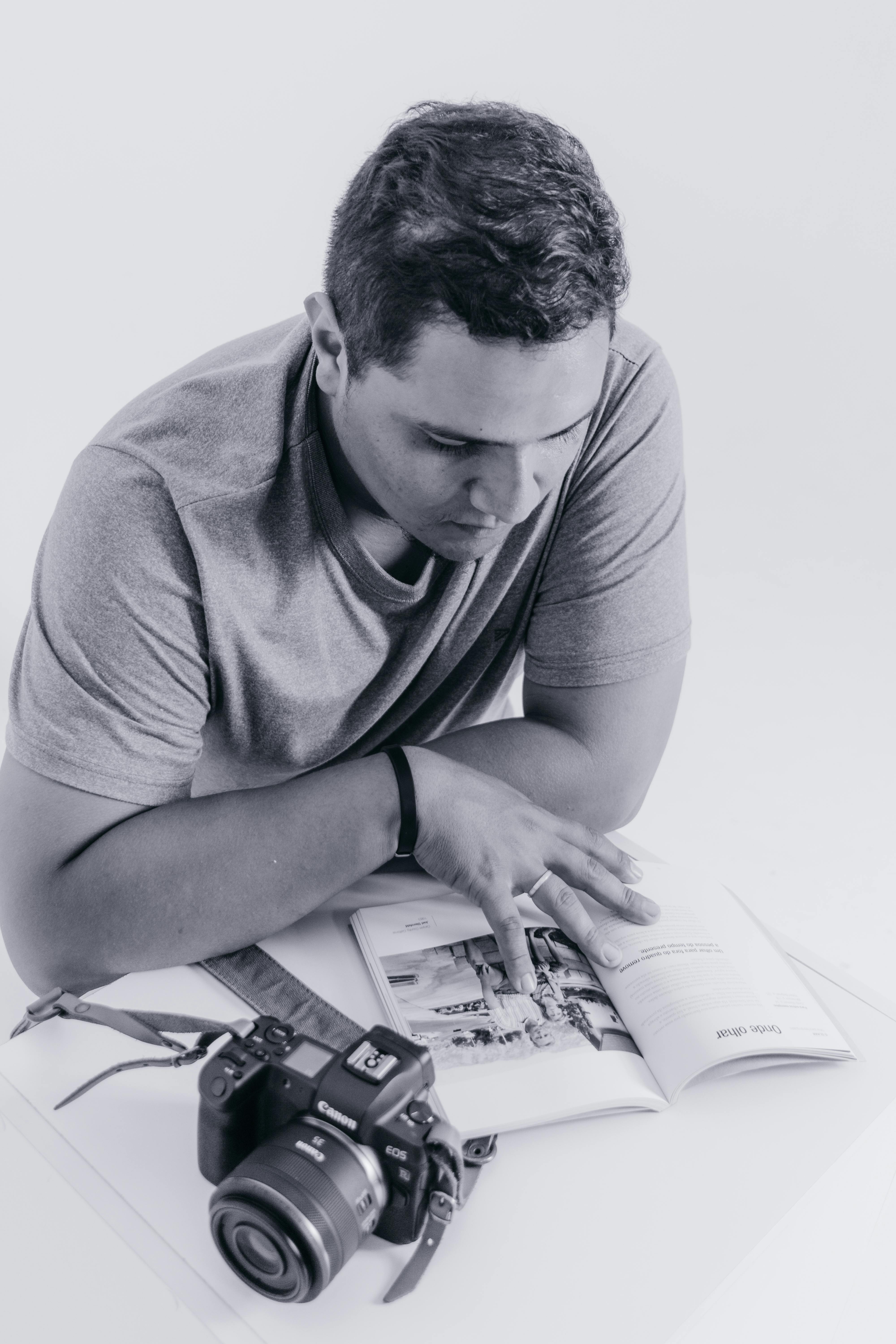 Monochrome photo of a man reading a book with a camera by his side, emphasizing contemplation and photography.