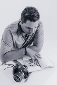 Monochrome photo of a man reading a book with a camera by his side, emphasizing contemplation and photography.