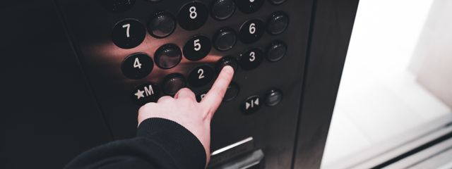 A person pressing the elevator button inside a modern elevator, showcasing the control panel with floor numbers.