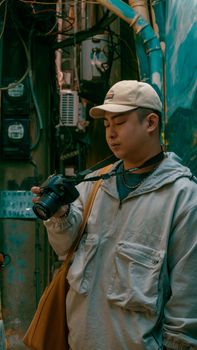 A man in casual attire with a camera explores an urban alley, capturing street photography.