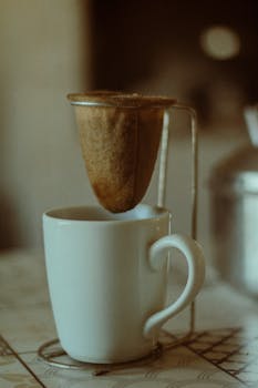 A traditional cloth coffee filter over a ceramic mug on a vintage table setting.