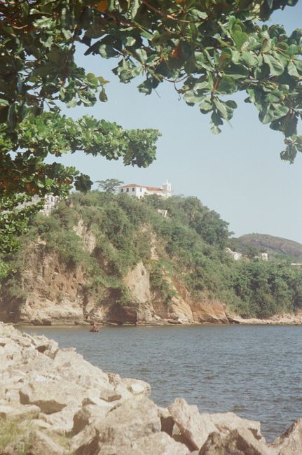 Serene coastal landscape with a house on a lush cliff under a clear sky.