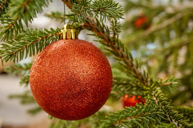 Close-up of a shimmering red Christmas ornament hanging on a lush pine branch, capturing festive holiday spirit.