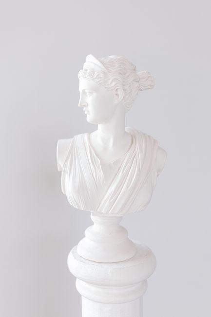 Classical white marble bust of a woman on a pedestal against a white background.