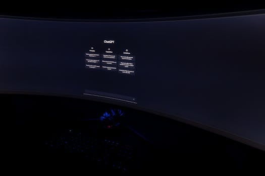 Close-up of a dark room with a curved monitor showing the ChatGPT interface on screen.