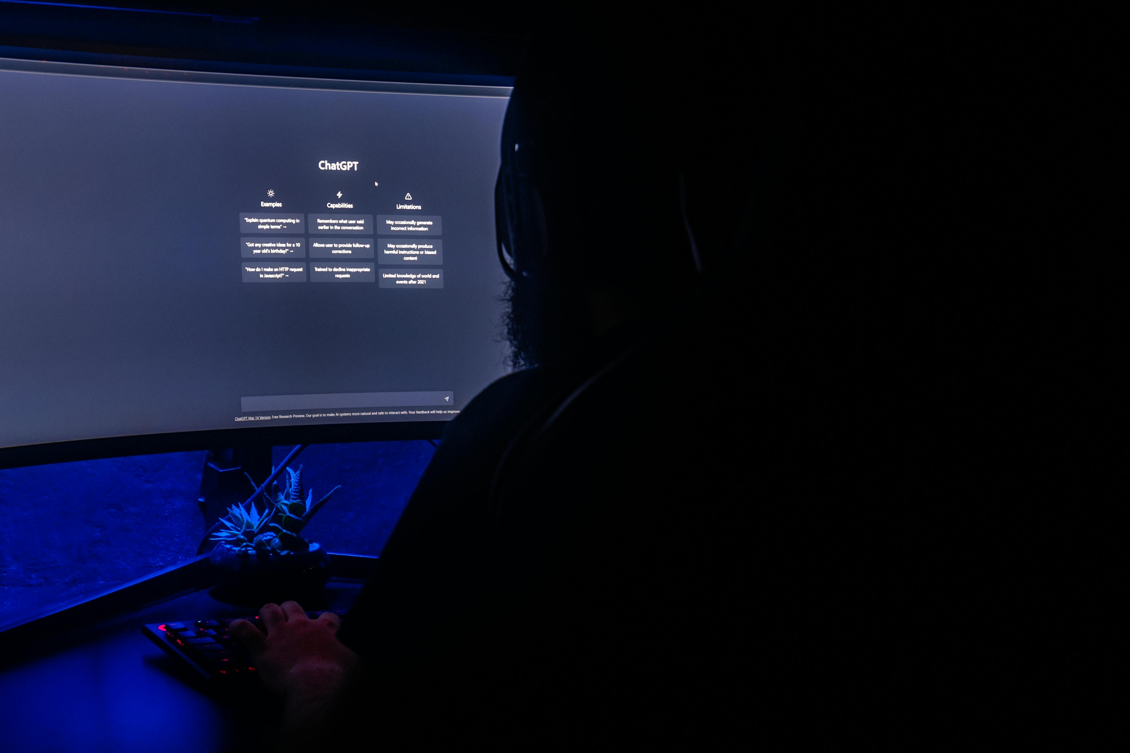 Silhouette of a person using ChatGPT on a computer screen in a dark room, highlighting digital interaction.