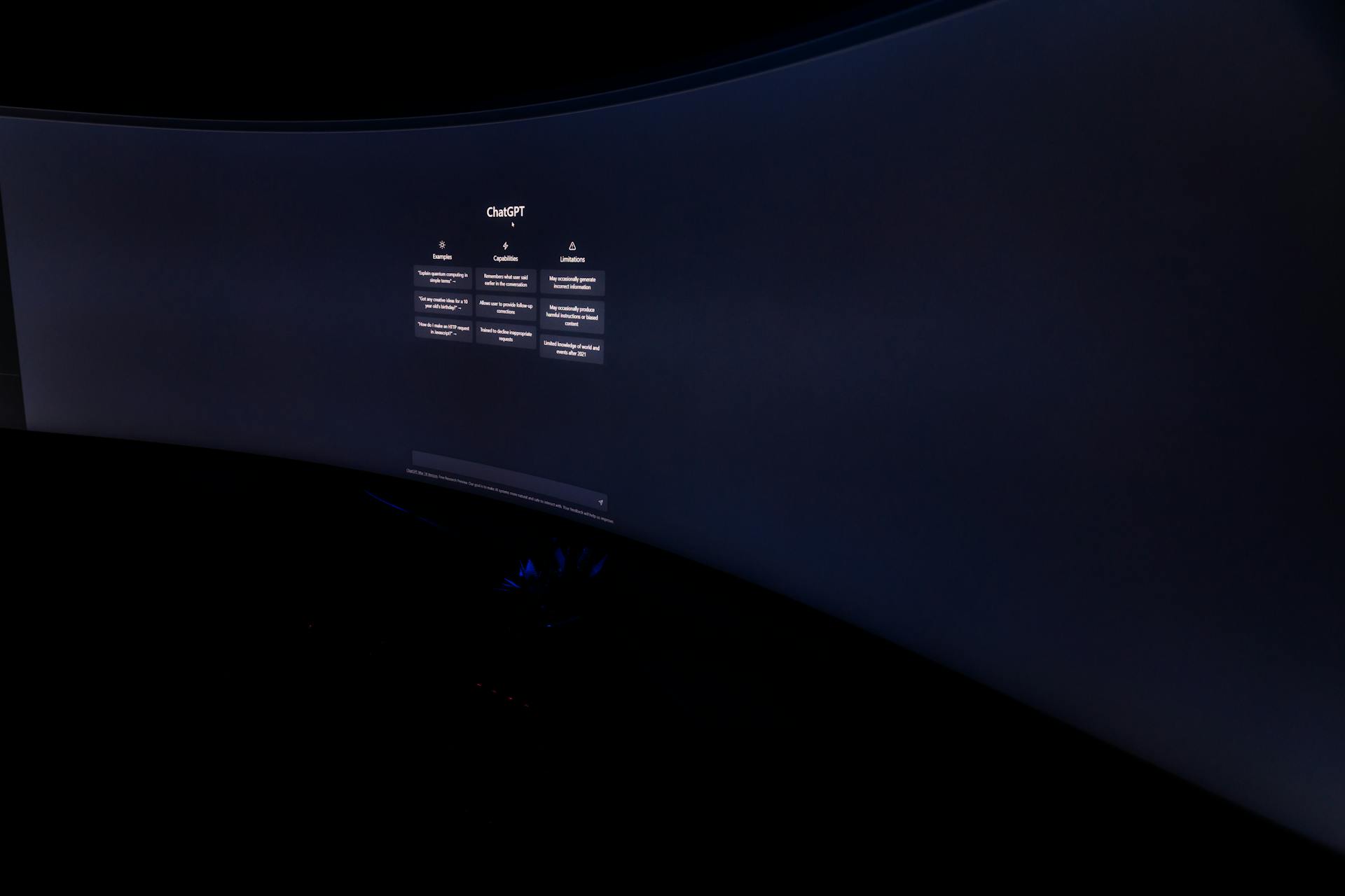 Curved monitor screen showing ChatGPT interface in low-light, focus on technology and AI.