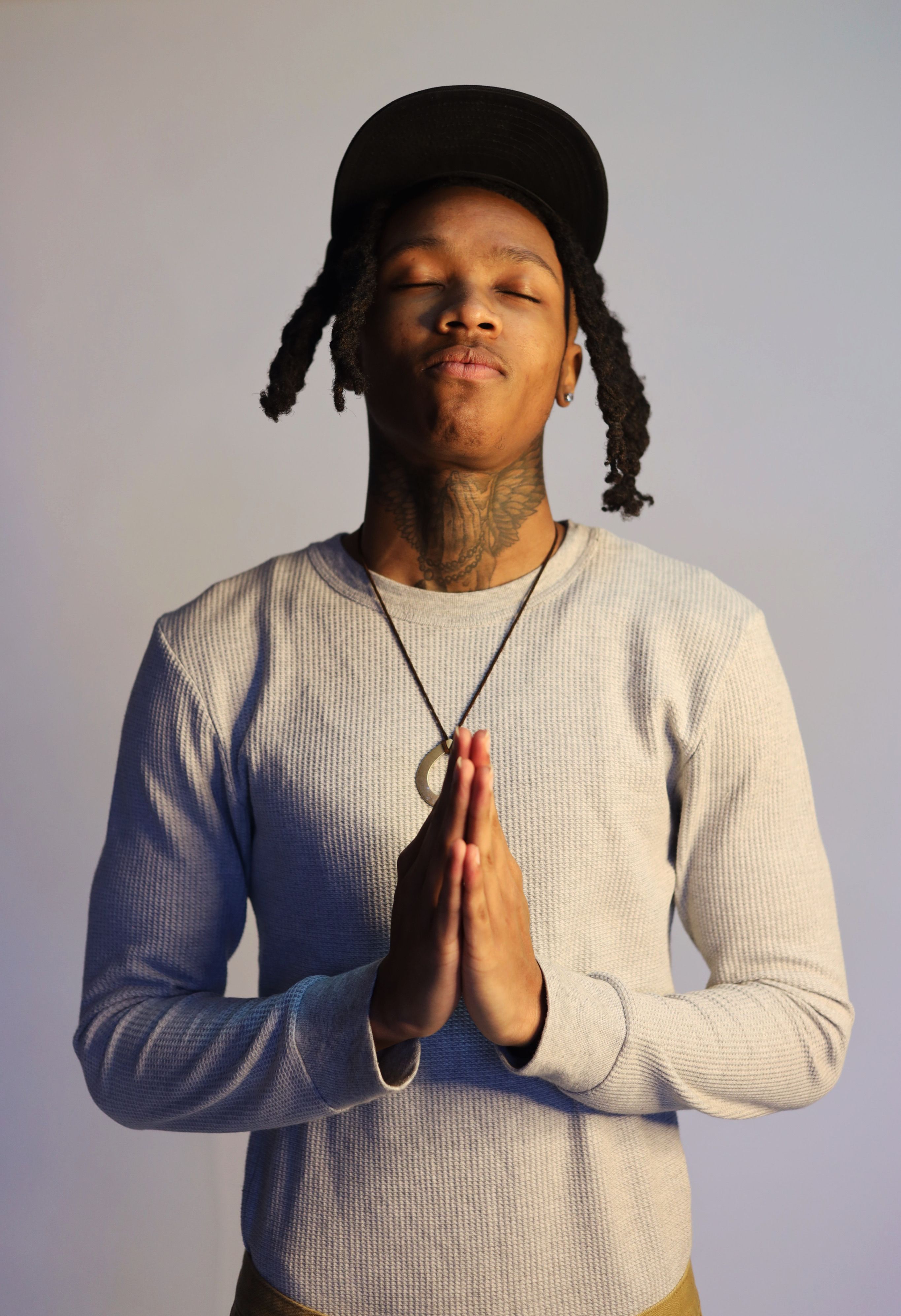 Young adult with tattoos standing with eyes closed, displaying a serene prayer pose.