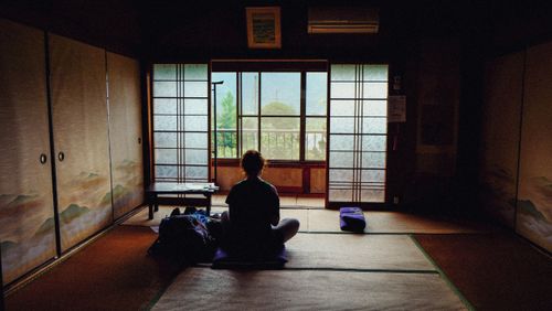 Free A person meditating in a tranquil traditional Japanese room, facing the view outside. Stock Photo