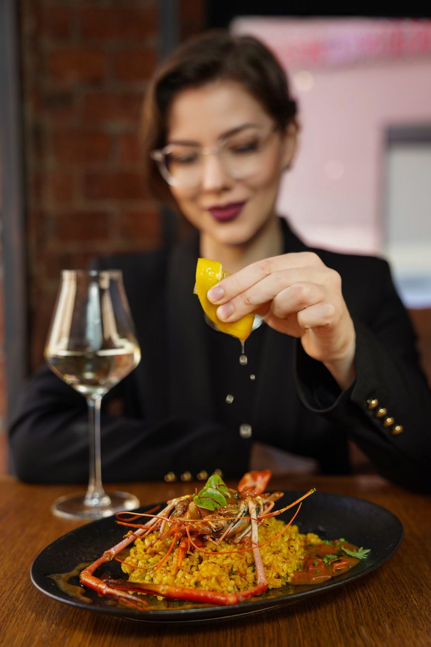 Elegant woman enjoying a gourmet seafood meal with lemon and wine indoors.