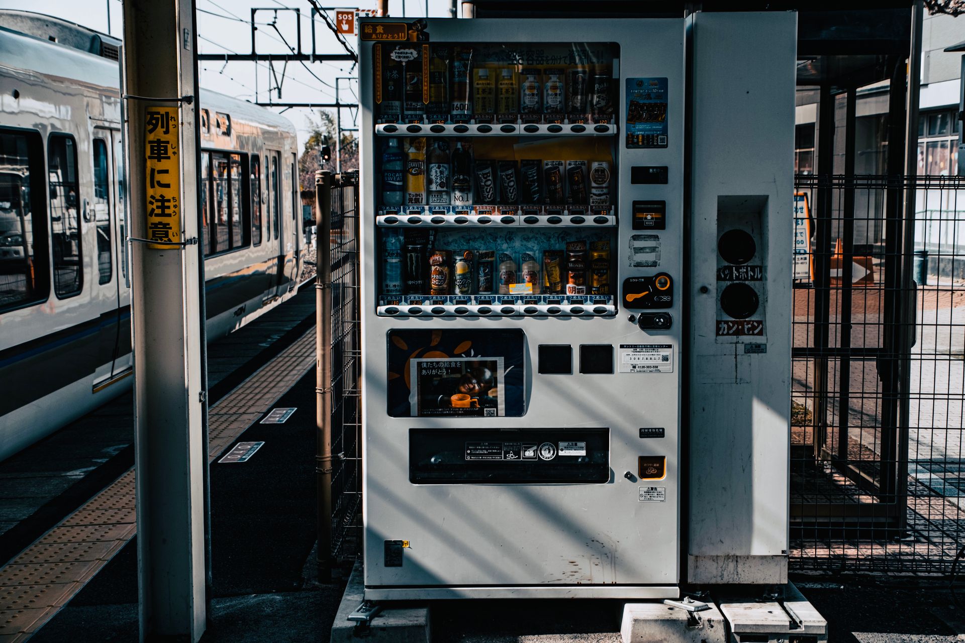 Vending machine stocked with beverages at an outdoor train station.