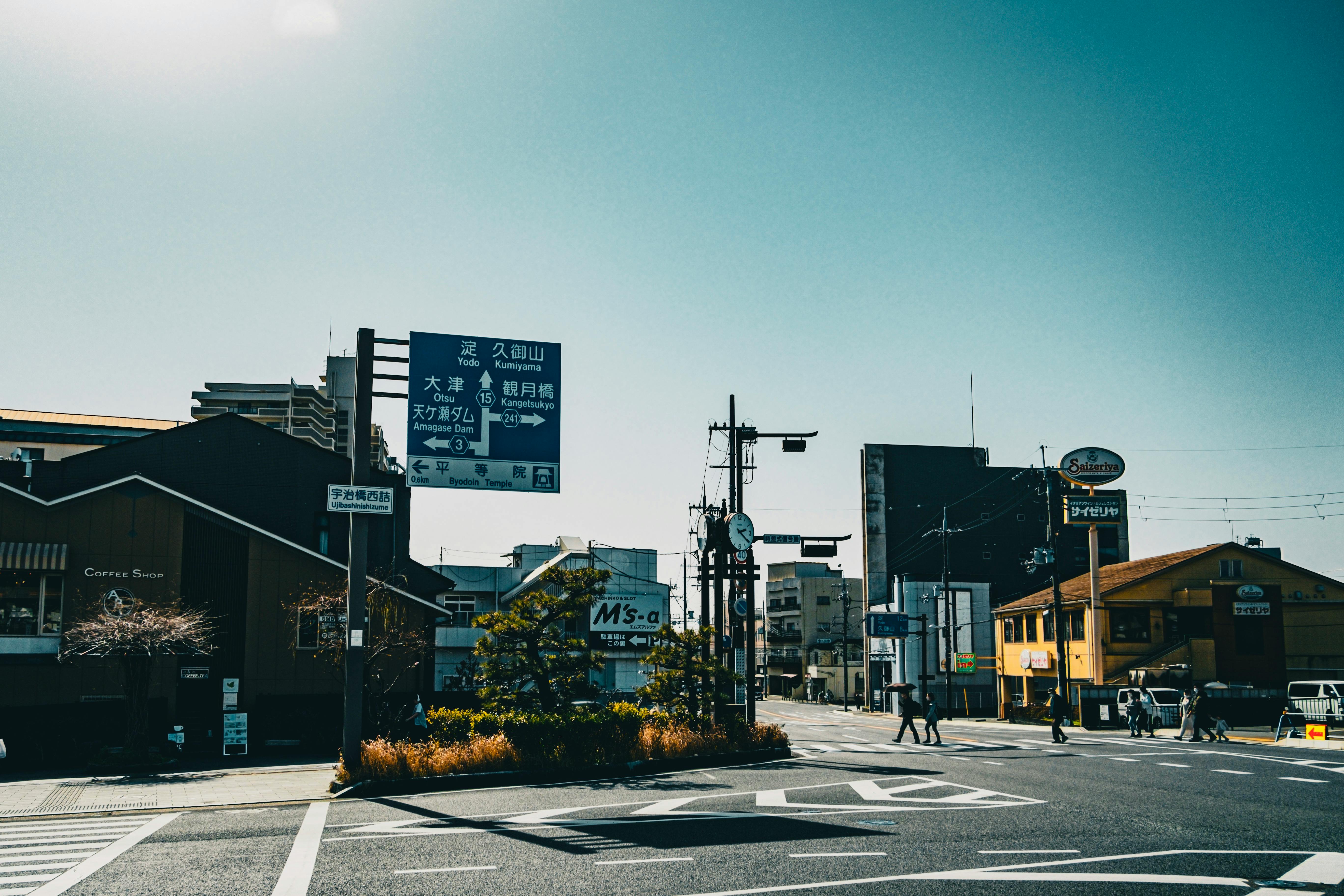 A city street scene featuring buildings, signage, and pedestrians under a bright sky.