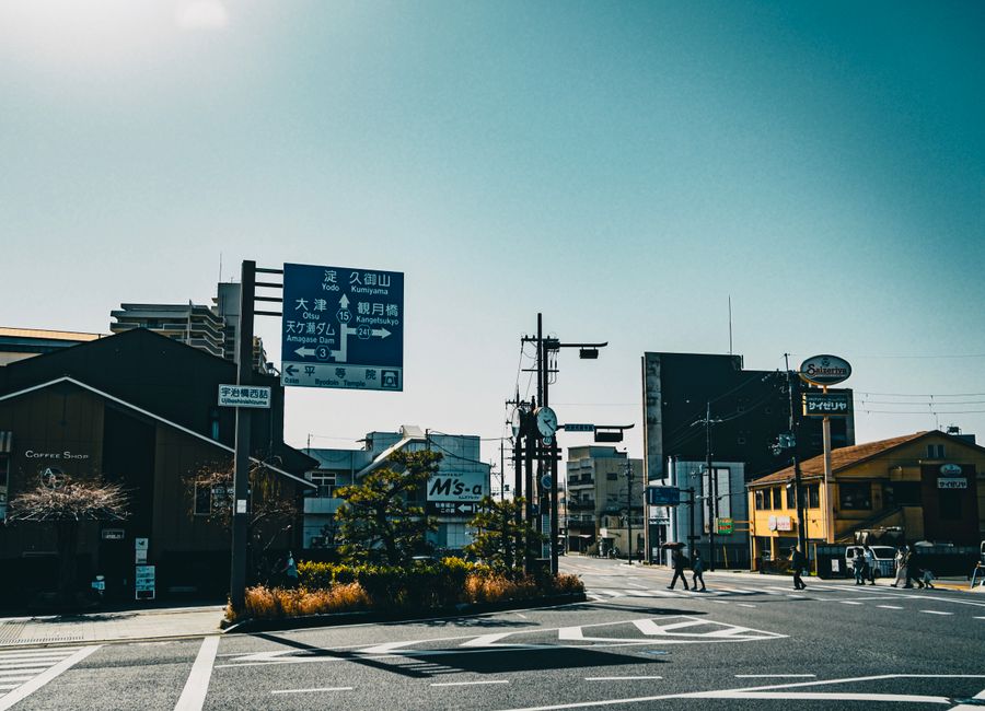 A city street scene featuring buildings, signage, and pedestrians under a bright sky.