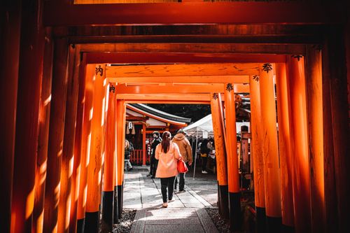 Free Visitors explore vibrant red torii gates at a traditional Shinto shrine in Japan. Stock Photo